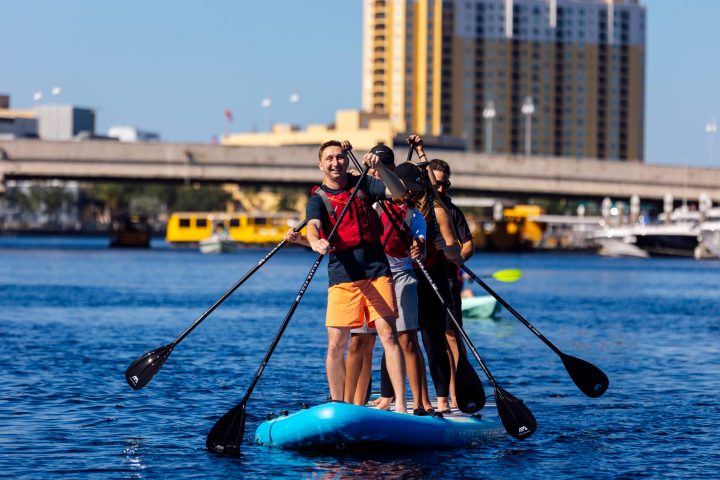 Three people paddleboarding on a river in a cityscape background.