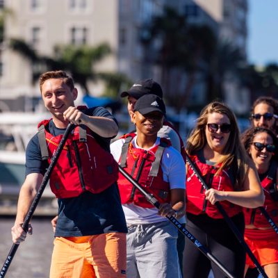 Group of people paddleboarding on water in red life vests.