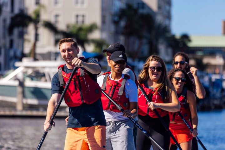 Group of people paddleboarding on water in red life vests.