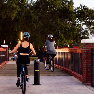 Two people biking on a brick bridge, surrounded by trees.