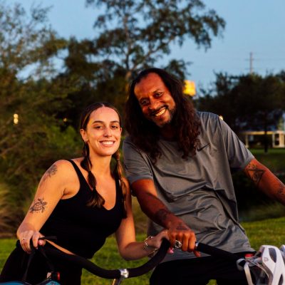 Two people smiling, leaning on bikes in a park setting.