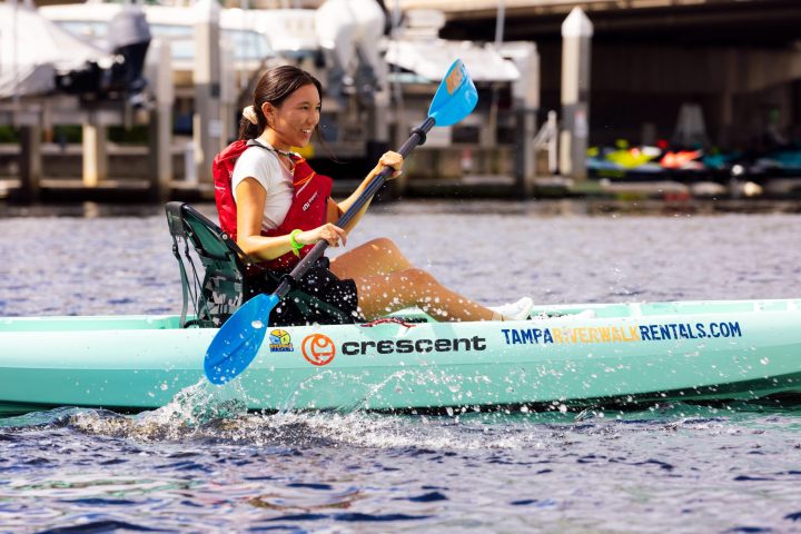 Person kayaking on water near a marina.