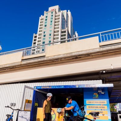 Family renting bikes near a blue kiosk with a tall building in the background.
