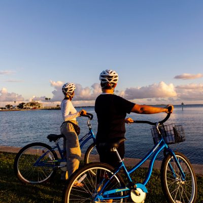Two cyclists wearing helmets admire a scenic waterfront view at sunset.