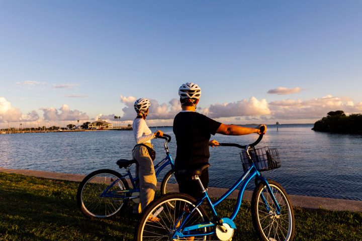 Two cyclists wearing helmets admire a scenic waterfront view at sunset.