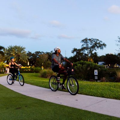 Two people biking on a park path surrounded by greenery.
