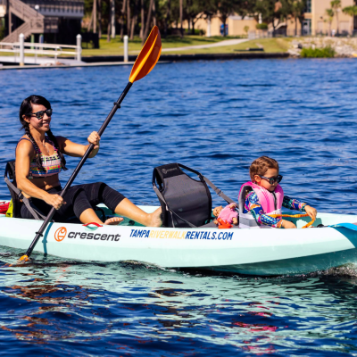 Woman and child kayaking on a sunny lake with calm blue water.