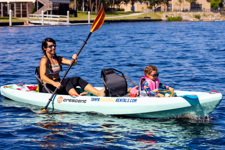 Woman and child kayaking on a sunny lake with calm blue water.