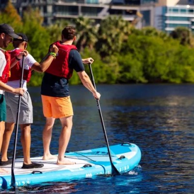 People paddleboarding on a calm river by a cityscape.
