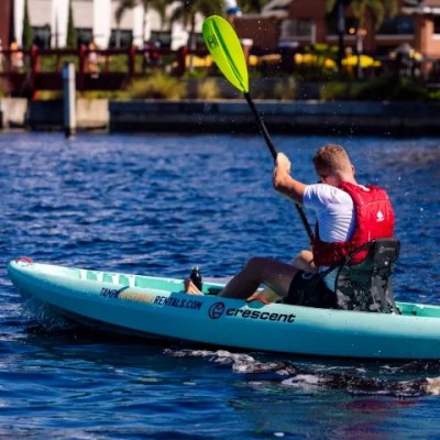 Person kayaking on a blue lake with colorful buildings in the background.